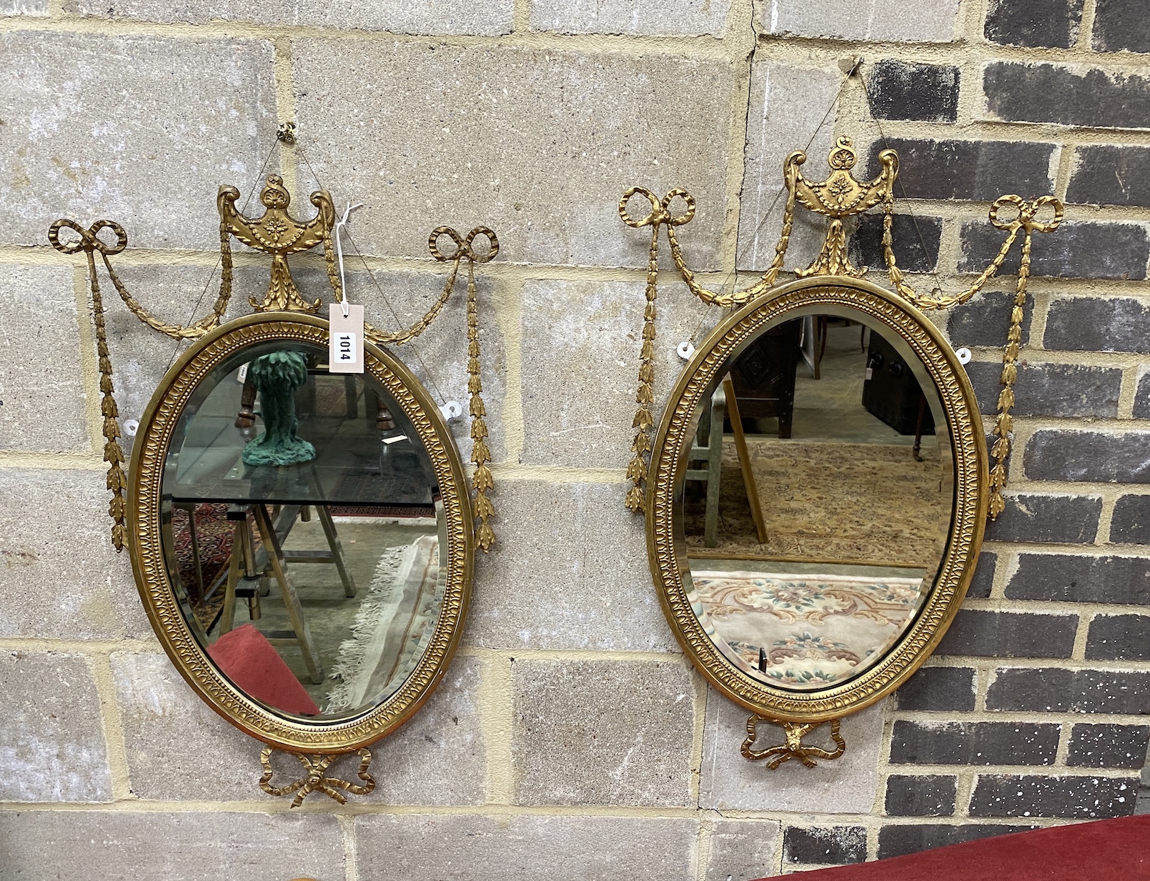 A pair of Edwardian Adam design giltwood and composition oval wall mirrors with swagged urn pediments, width 42cm, height 74cm